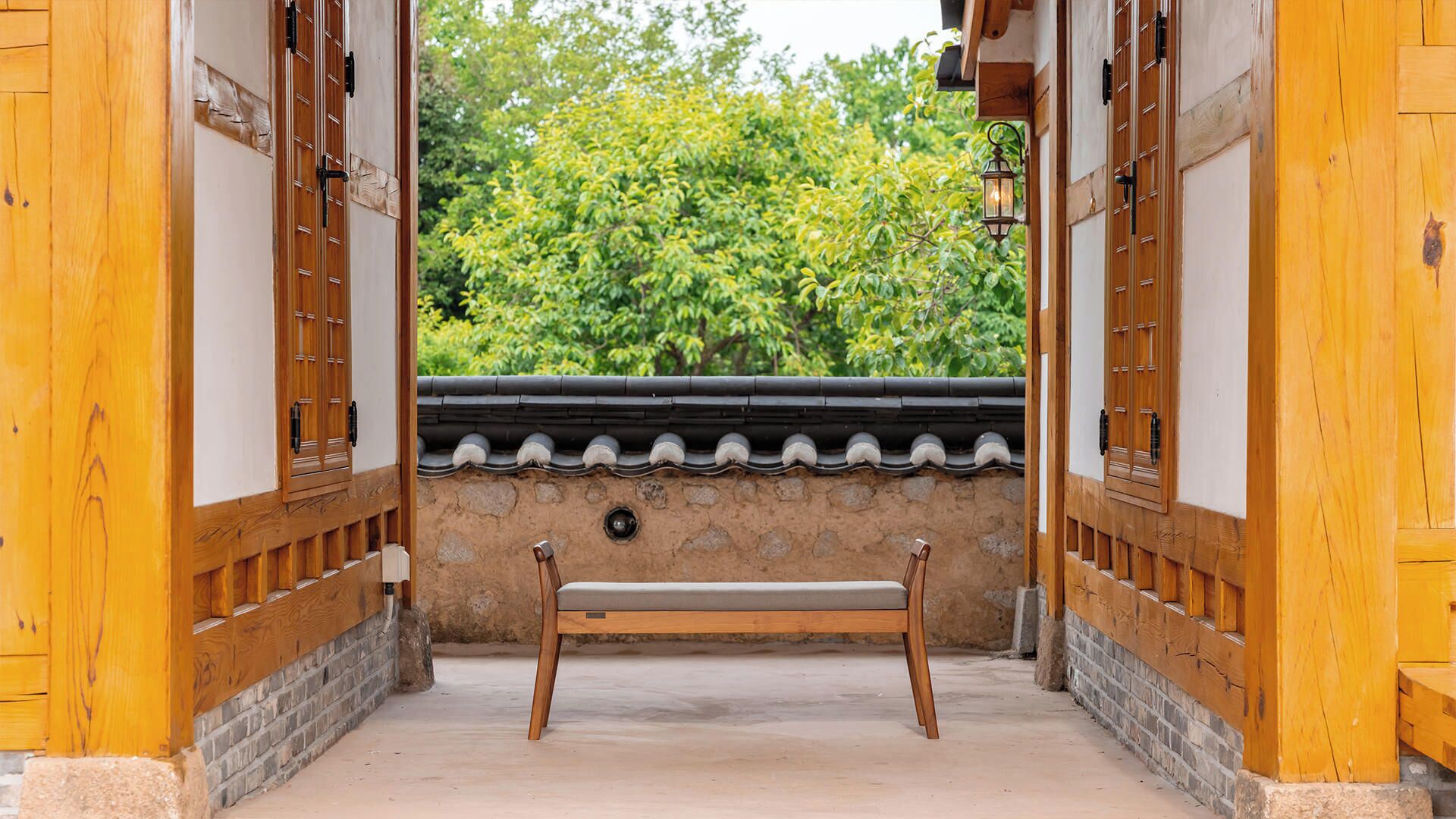 A traditional wooden gate leading to a stone wall with a bench in the center.