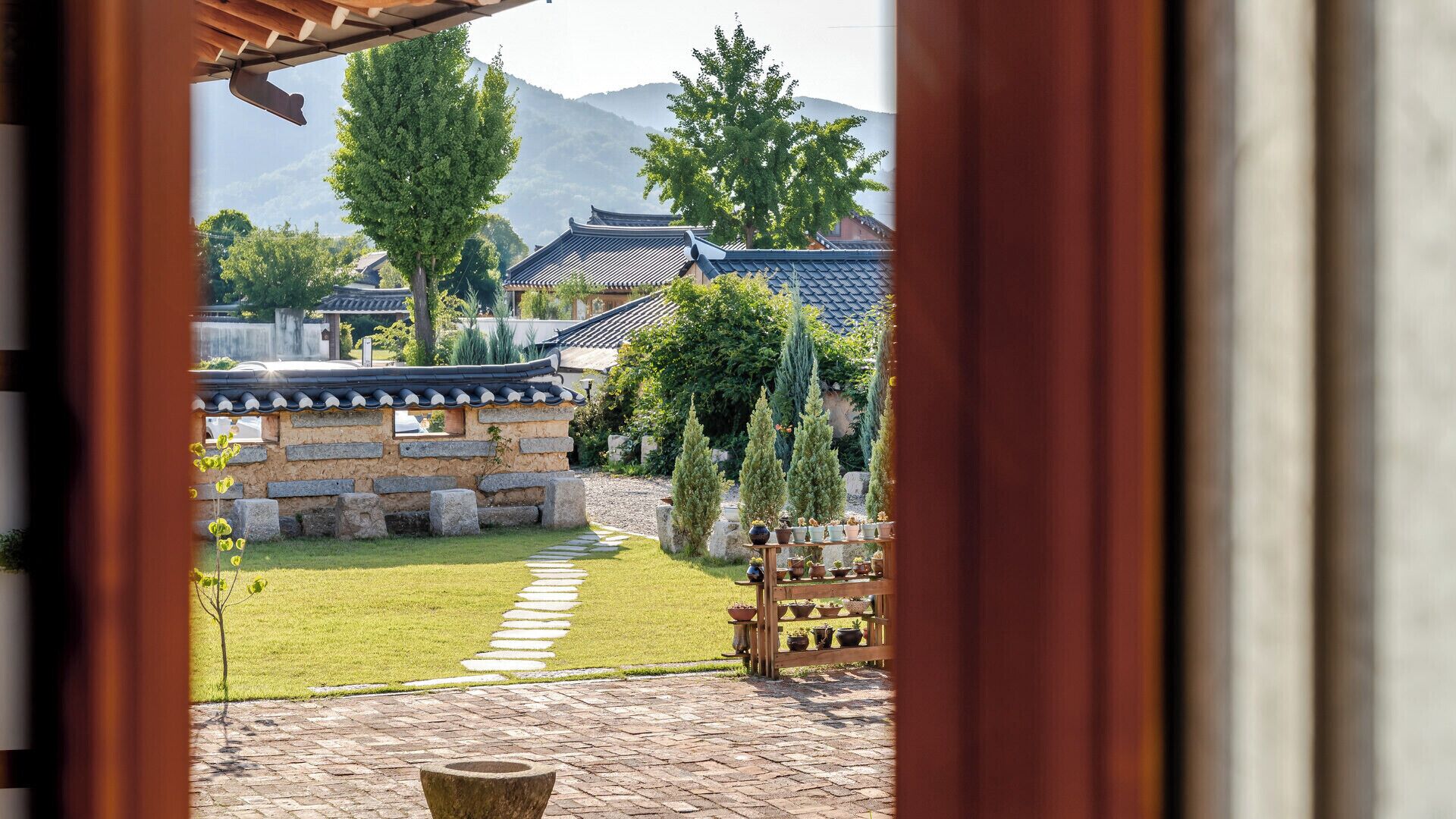 A traditional Korean courtyard with stone walls, a stone pathway, and potted plants.