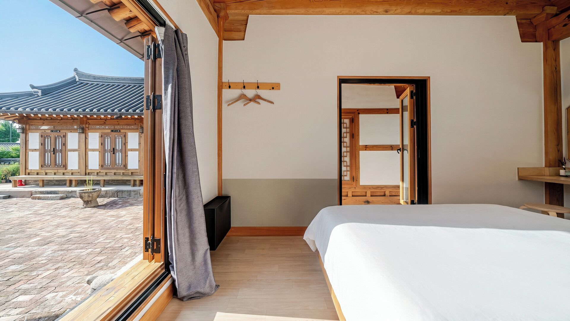 A bedroom with a large bed, a wooden floor, a window with curtains, and a view of a traditional building outside.
