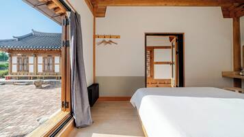 A bedroom with a large bed, a wooden floor, a window with curtains, and a view of a traditional building outside.