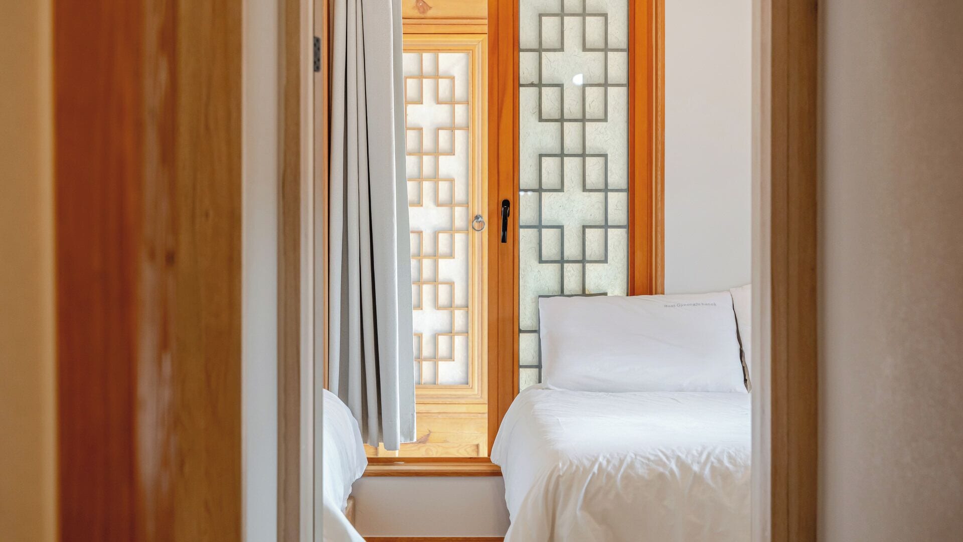 A narrow hallway leading to a bedroom with a bed, a wooden door, and a frosted glass partition.