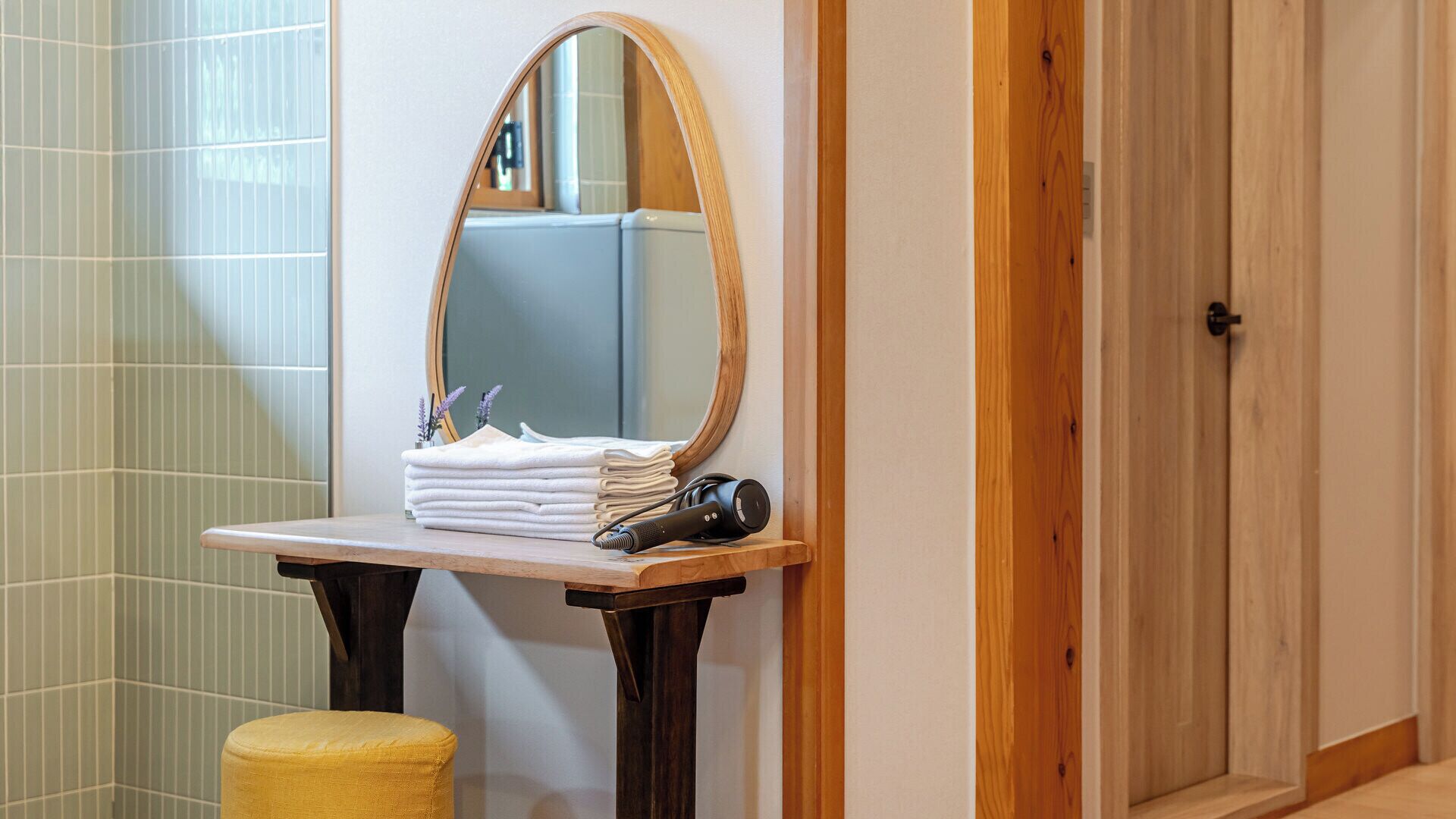 Un baño con tocador de madera, un espejo, una pila de toallas y un taburete amarillo.