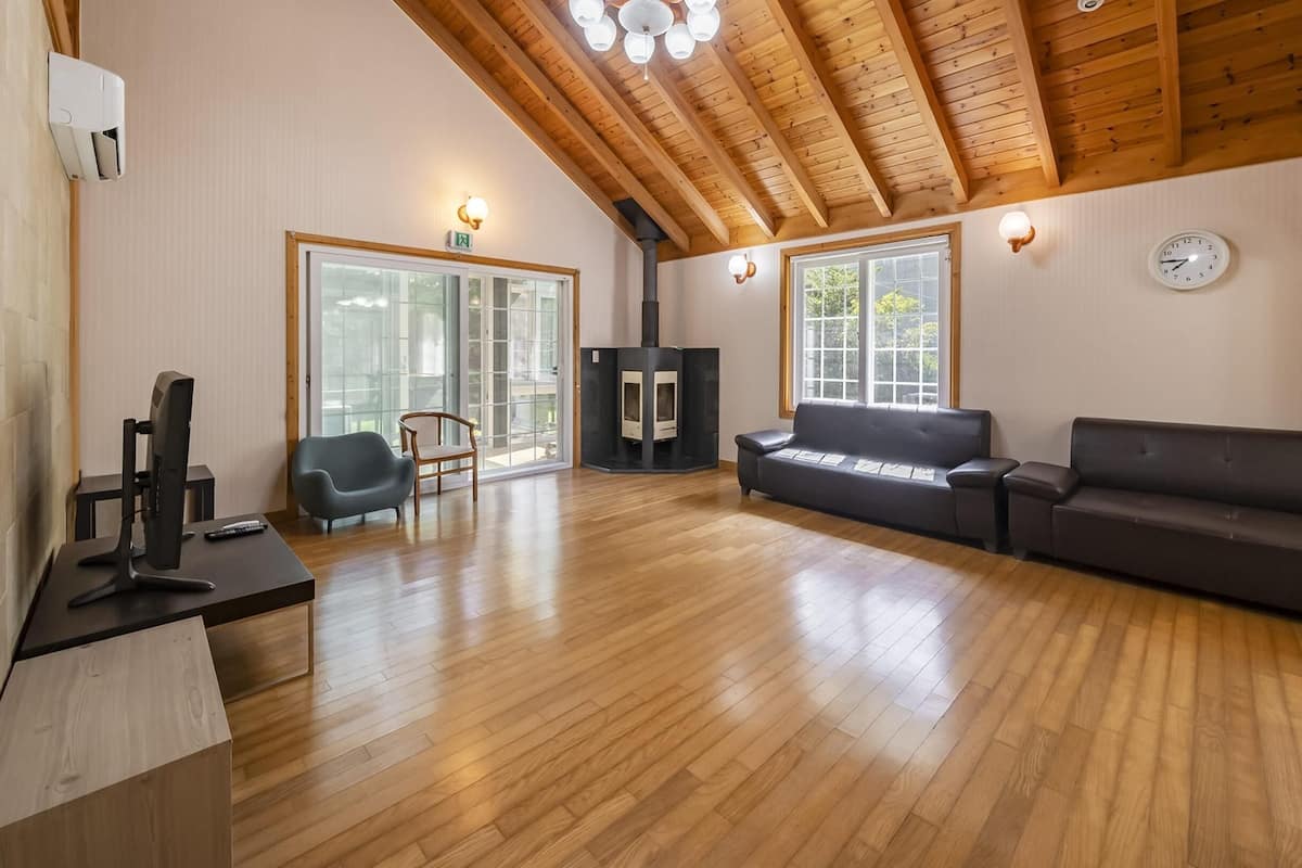 A spacious living area with wooden flooring, a fireplace, a sofa, a chair, and a television.