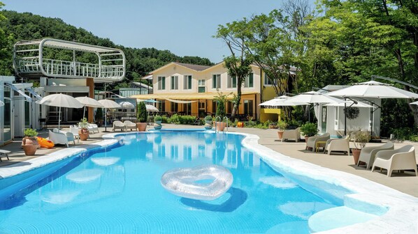 A swimming pool with a heart-shaped float, surrounded by outdoor seating and umbrellas, with a building in the background. - Yangpyeong Seojongpool pet Pension (Yangpyeong)
