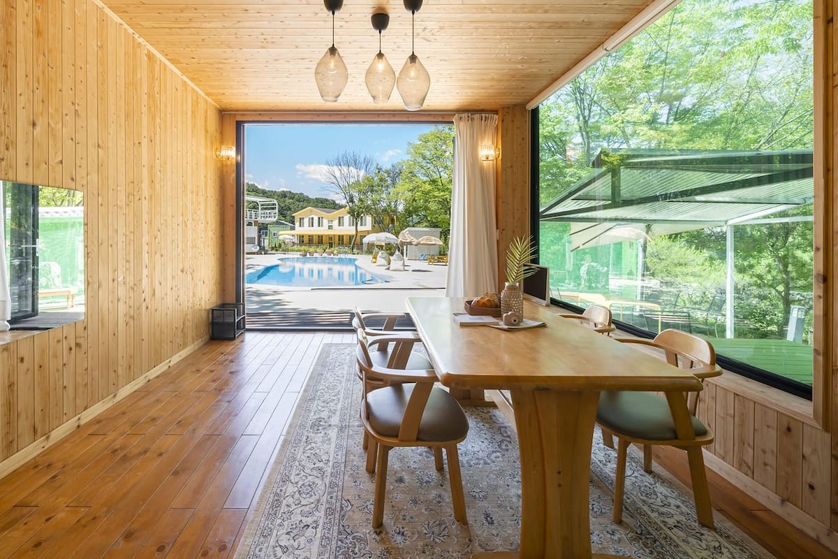 A wooden interior with a dining area, large windows, and a view of a swimming pool and outdoor area.