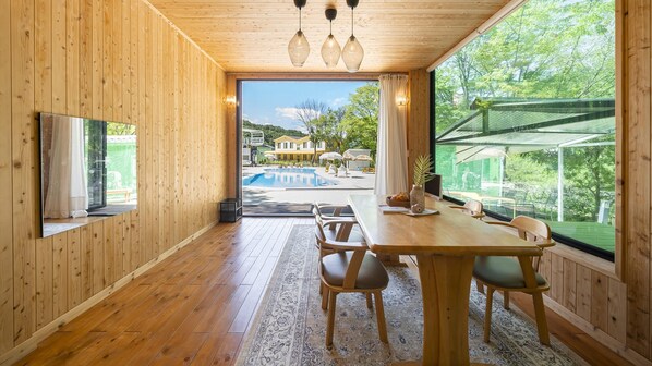 A wooden interior with a dining area, large windows, and a view of a swimming pool and outdoor area. - Yangpyeong Seojongpool pet Pension (Yangpyeong)