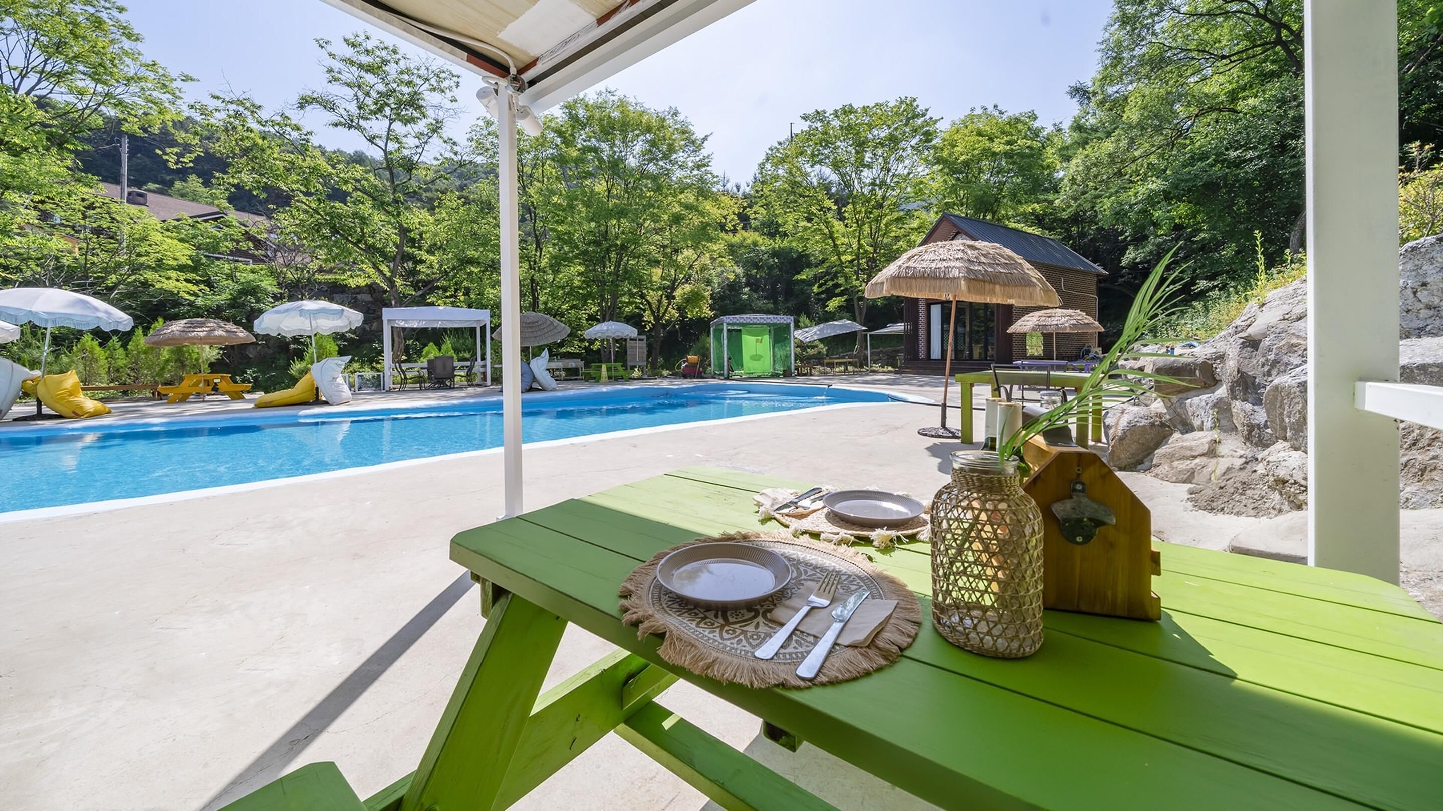A poolside area with a table set for dining, surrounded by umbrellas and lounge chairs.