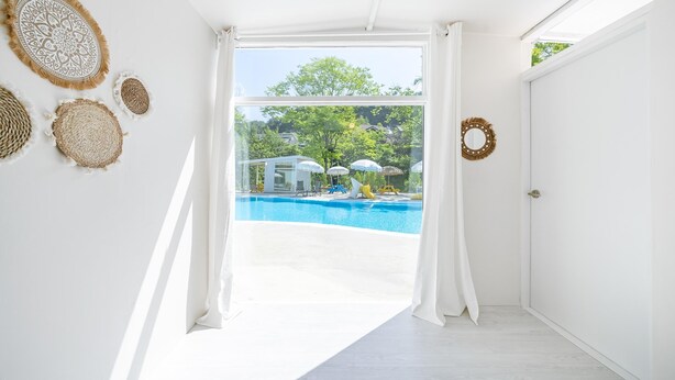 A bright room with a large window leading to a pool area, featuring white walls, a wooden floor, and decorative woven wall hangings. - Yangpyeong Seojongpool pet Pension (Yangpyeong)