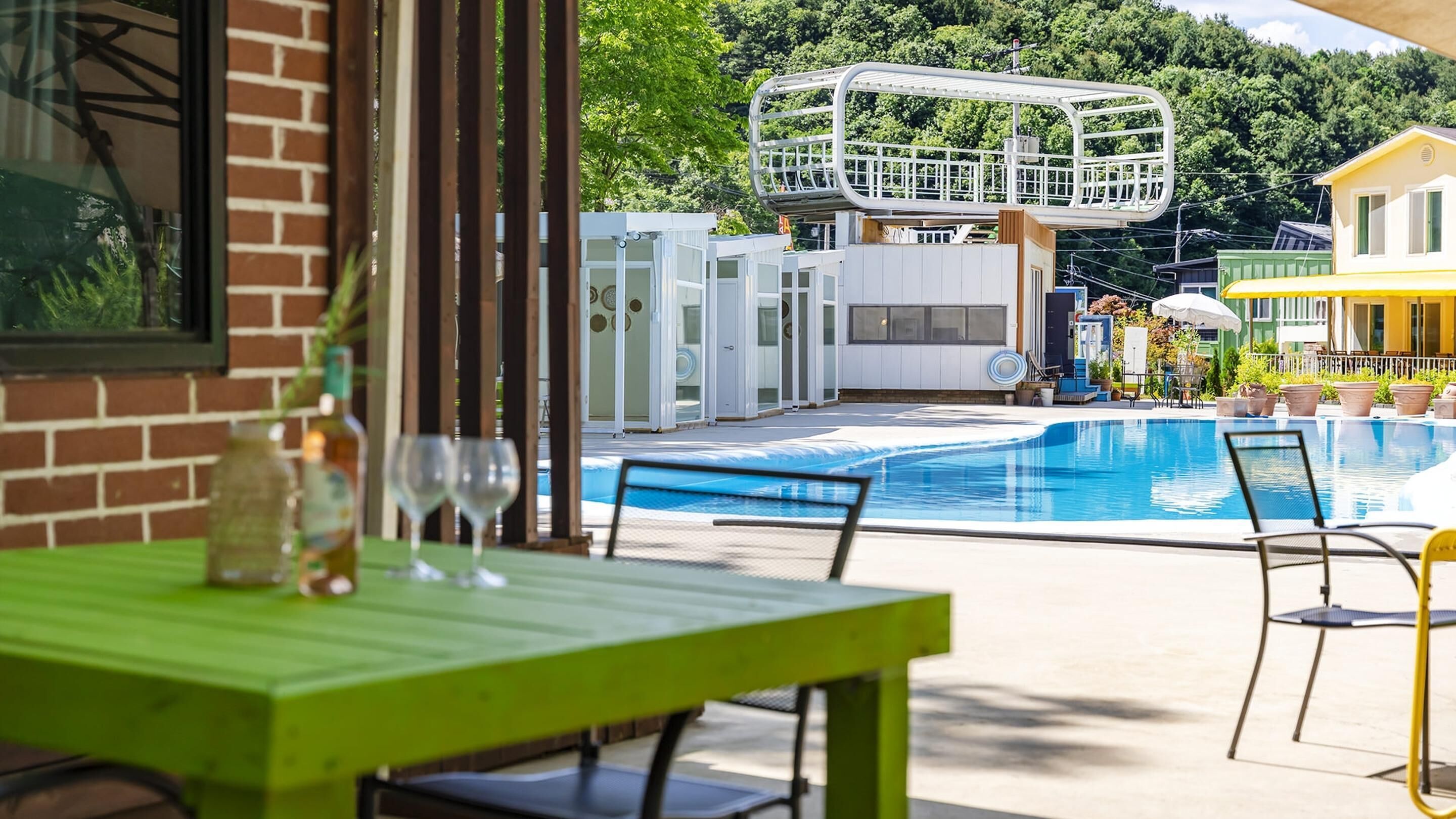 A pool area with a clear view of the pool, a green table, and a white structure in the background.