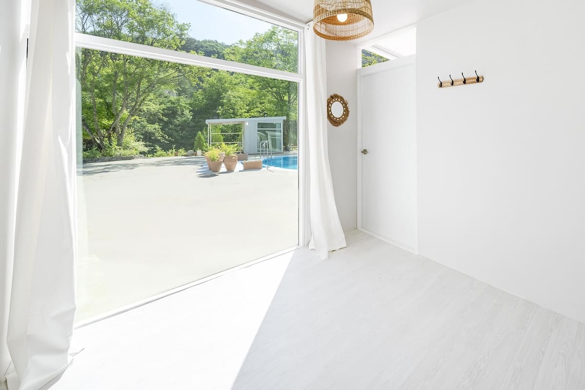 A bright room with a large window, white walls, and a wooden floor.