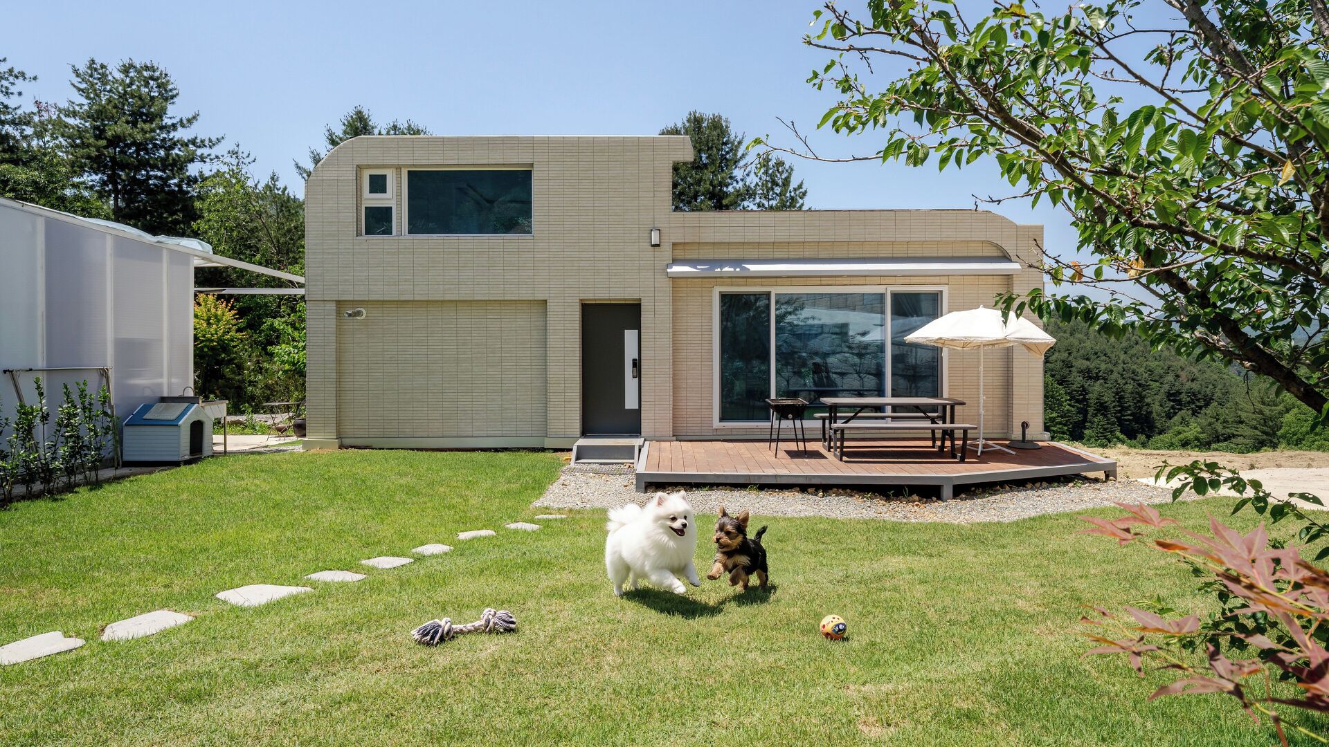 Una casa moderna de dos pisos con un patio, una caseta para perros y un pequeño jardín.