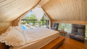 A cozy, wooden-roofed bedroom with a large bed, a comfortable armchair, and a view of an outdoor swimming pool. - Yangpyeong Seojongpool pet Pension (Yangpyeong)
