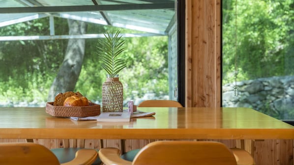 Una mesa de madera con una cesta de pan tejida y un florero de vidrio con una planta.