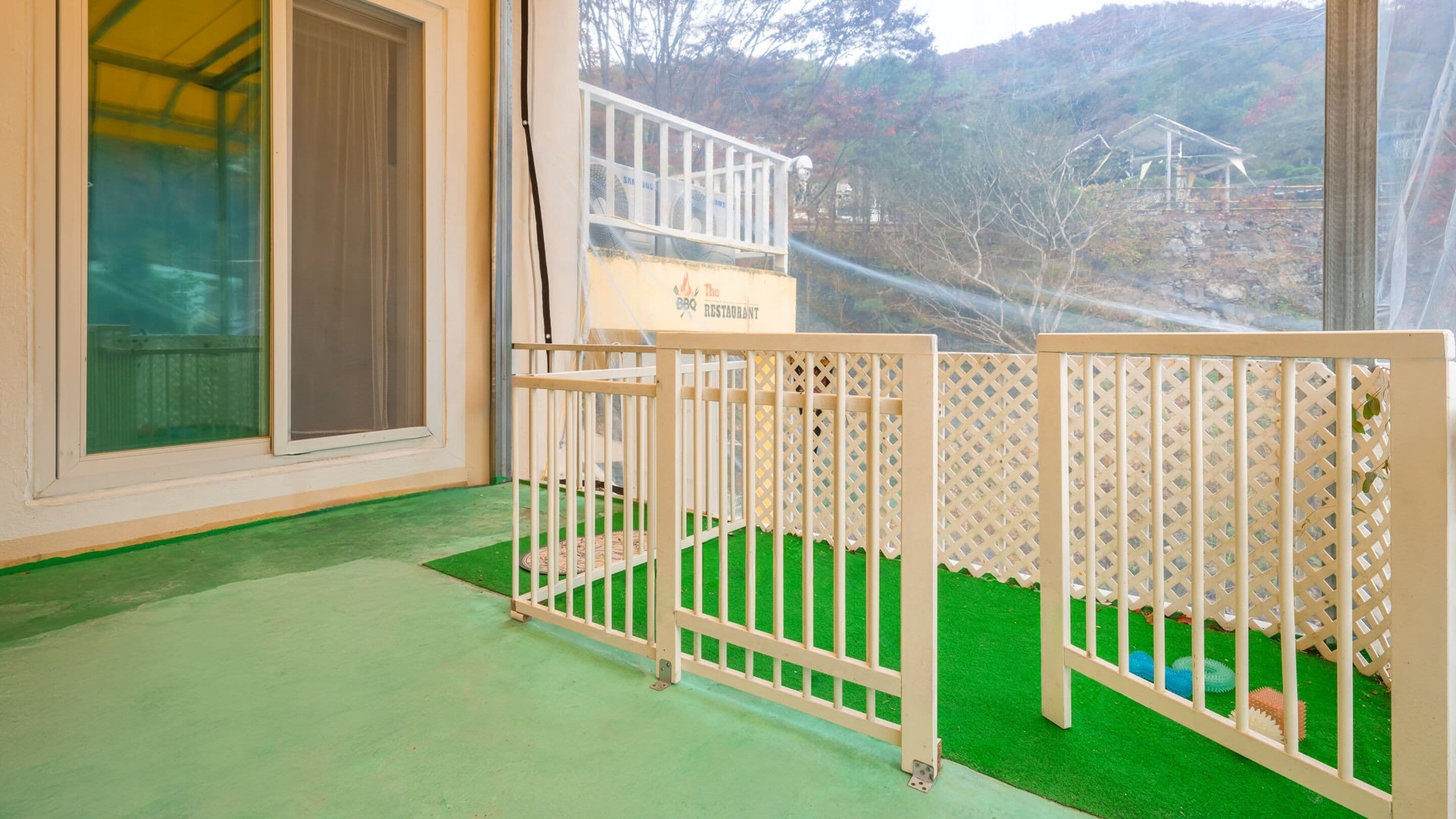 Ein Zimmer mit Blick auf eine gebirgige Landschaft, ein Balkon mit Schild für ein Grillrestaurant und eine begrünte Rasenfläche.