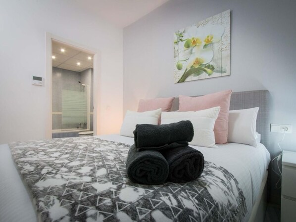 A neatly made bed with rolled towels, a patterned bedspread, and a wall-mounted artwork of flowers.
