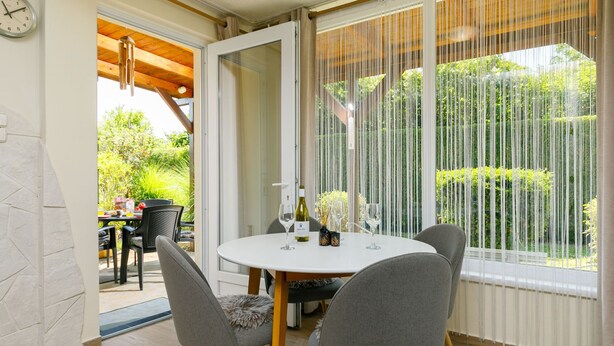 A dining area with a round table, four chairs, and a view of a garden through large windows. - Vacation home Lupo by Interhome (Balatonboglar)