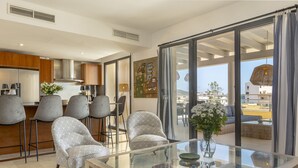 Una sala de estar moderna con una mesa de centro de vidrio, sillones estampados y vistas de la ciudad a través de amplios ventanales correderas.