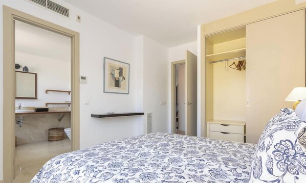 A bedroom with a bed, a bedside table, a mirror, a wardrobe, and a bathroom visible through an open door. - Cala Ventura by Mallorca North Villas (Port de Pollença)