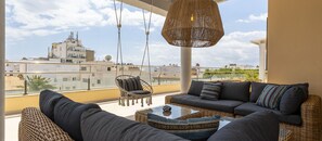 A balcony with wicker furniture, a hanging light fixture, and a view of buildings in the distance. - Cala Ventura by Mallorca North Villas (Port de Pollença)