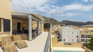 Una terraza en la azotea con sillones de descanso, piscina y vistas a la ciudad y montañas.