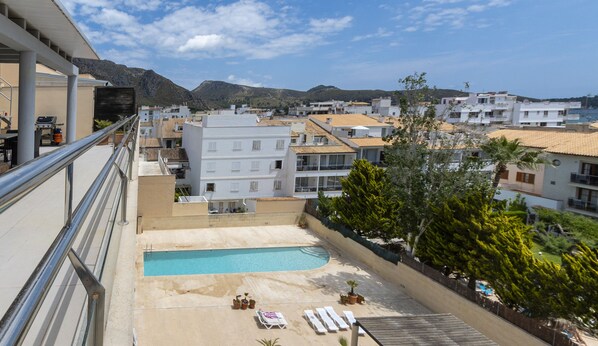 A pool area with lounge chairs and potted plants, surrounded by buildings and a mountainous backdrop. - Cala Ventura by Mallorca North Villas (Port de Pollença)
