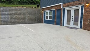 En parkeringsplats med två garageportar, en mur av tegelsten och två blå soptunnor.