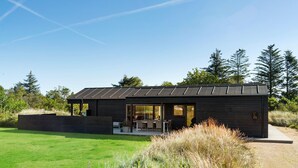 Une maison moderne à l’extérieur sombre, dotée d’une grande porte vitrée et d’un patio aménagé avec du mobilier d’extérieur.