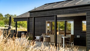 A modern wooden building with a patio area featuring outdoor seating and a hot tub.