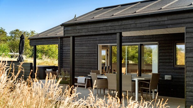 Un bâtiment moderne en bois doté d’un patio comprenant un espace extérieur avec des sièges et un jacuzzi.