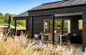 A modern wooden building with a patio area featuring outdoor seating and a hot tub. - Stunning home in ålbæk with sauna (Ålbæk)