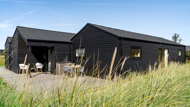 A black wooden cabin with a patio area, a table, and chairs.