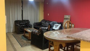 A living room with a red wall, two sofas, a coffee table, and a dining table with chairs. - Departamento Amplio Frente Parque Sarmiento 1 Cuadra a Terminal y Centro (Córdoba)