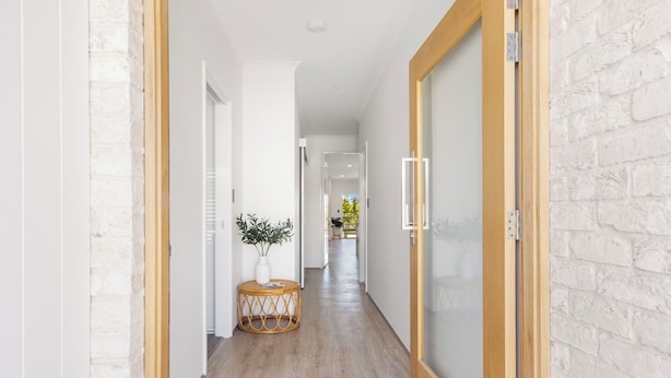 A hallway with a wooden floor, white walls, and a brick accent wall. - Newly Built Luxury Modern Home (Dunsborough)