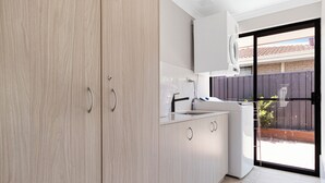 Een moderne keuken met lichte houten kastjes, een inbouwoven en een groot raam met uitzicht op de achtertuin.
