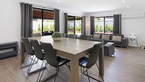 Een ruime kamer met een grote eettafel, grijze banken en uitzicht op het omliggende landschap.