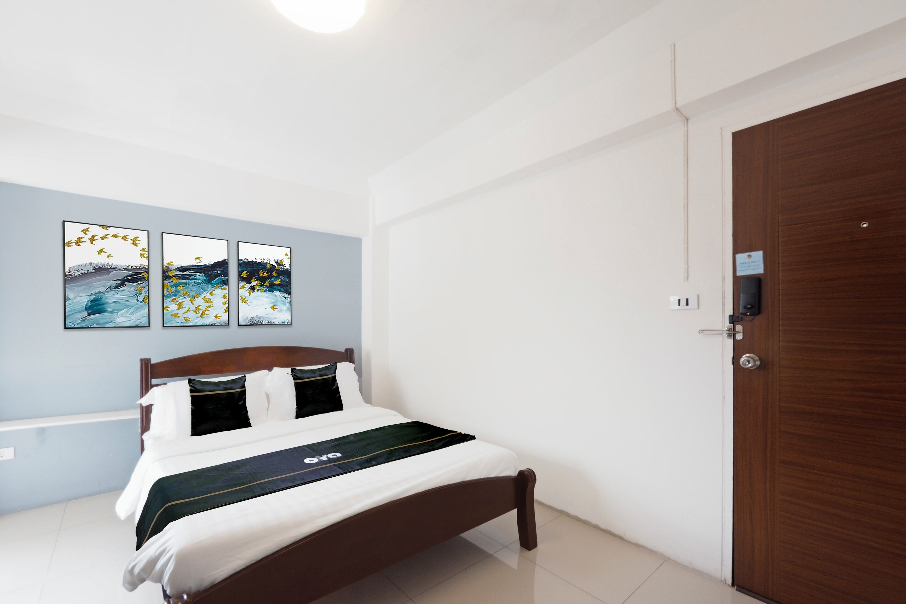 A bedroom with a bed, a wooden door, and three wall-mounted artworks.