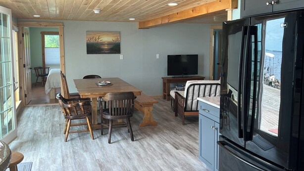 A spacious living area with a wooden ceiling, a dining table with chairs, a black refrigerator, and a television.