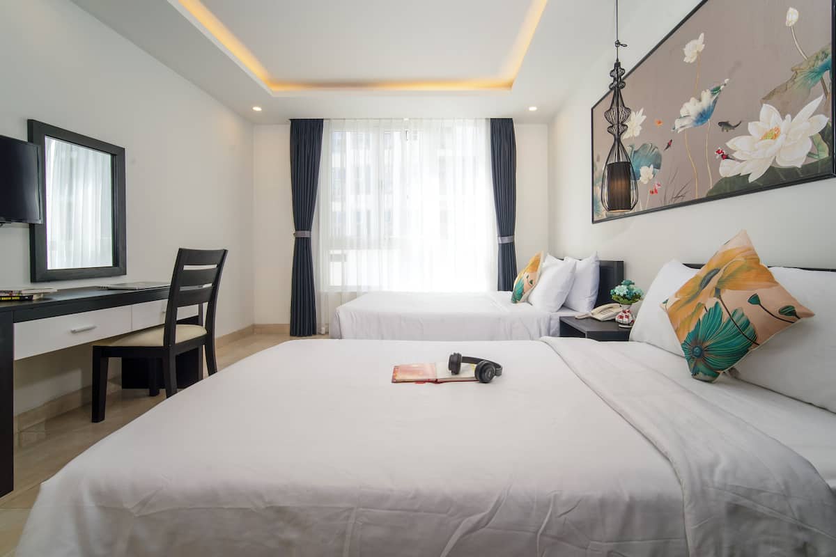 Quarto de hotel com cama, escrivaninha, cadeira, televisão e um quadro na parede.