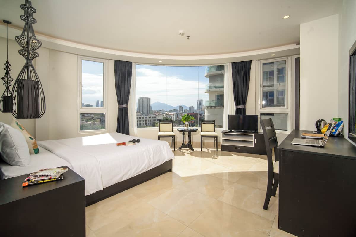 Quarto de hotel moderno com uma cama grande, escrivaninha, televisão e vista para a cidade.