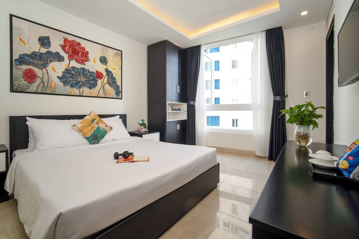 Quarto de hotel moderno com uma cama grande, uma televisão de tela plana, uma mesa com uma planta e uma janela com cortinas.