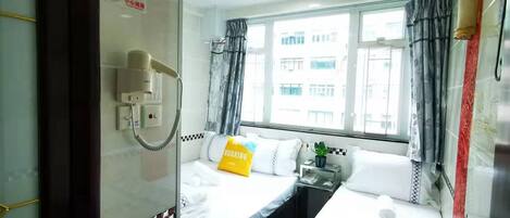 Quarto de hotel com duas camas, uma janela com cortinas, um ventilador de teto e um telefone na parede.