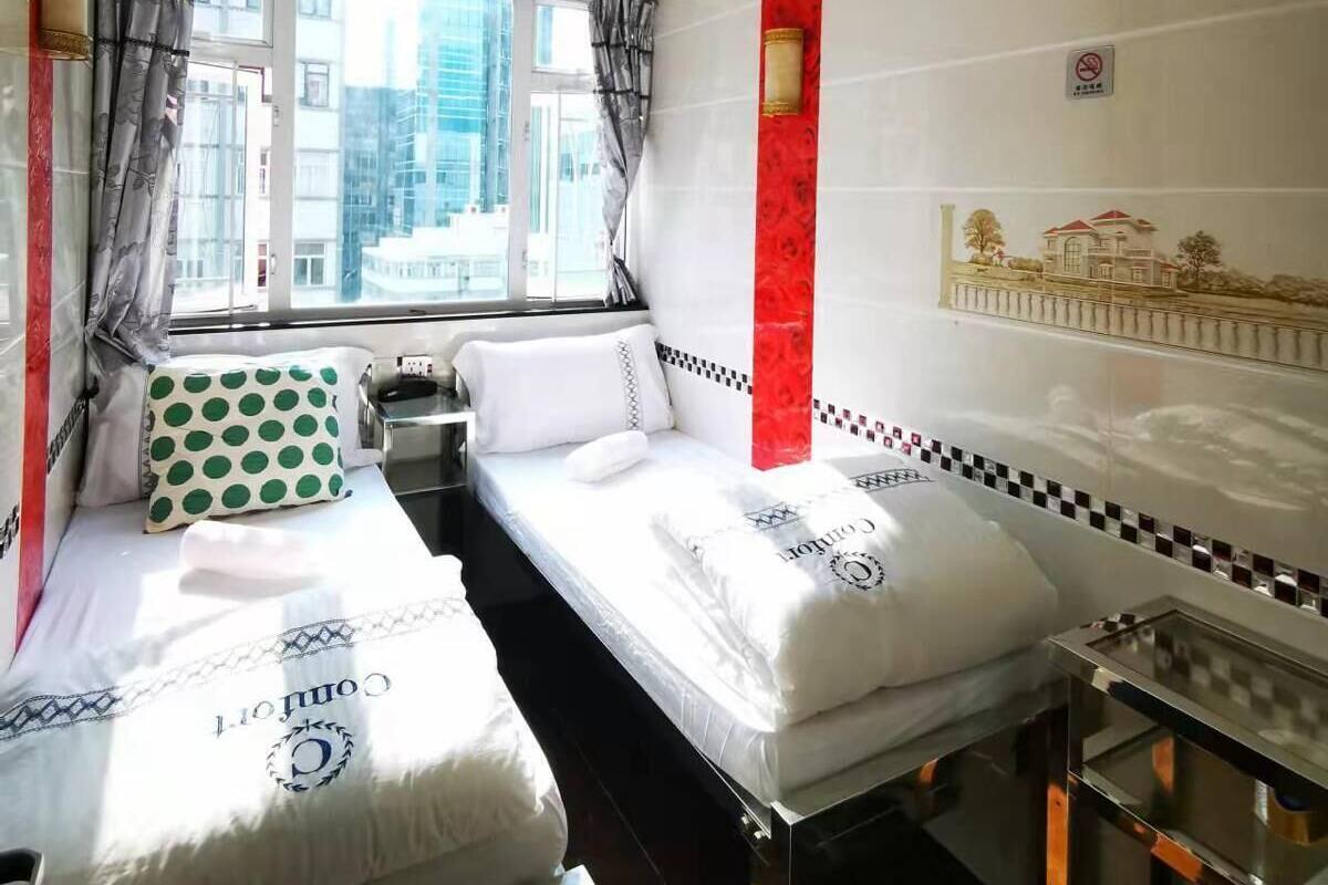 Ein Hotelzimmer mit zwei Betten, einem Vorhangfenster, einer roten Akzentwand und einem kleinen Tisch.