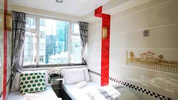 A hotel room with two beds, a window with curtains, a red accent wall, and a small table.