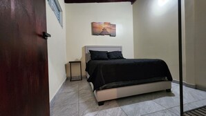 Une chambre à coucher avec un lit, une table de chevet, un tableau accroché au mur et une porte.