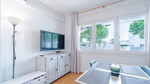 Un salon moderne avec un téléviseur à écran plat, une table à manger avec un set de table, un meuble blanc et une lampe sur pied.