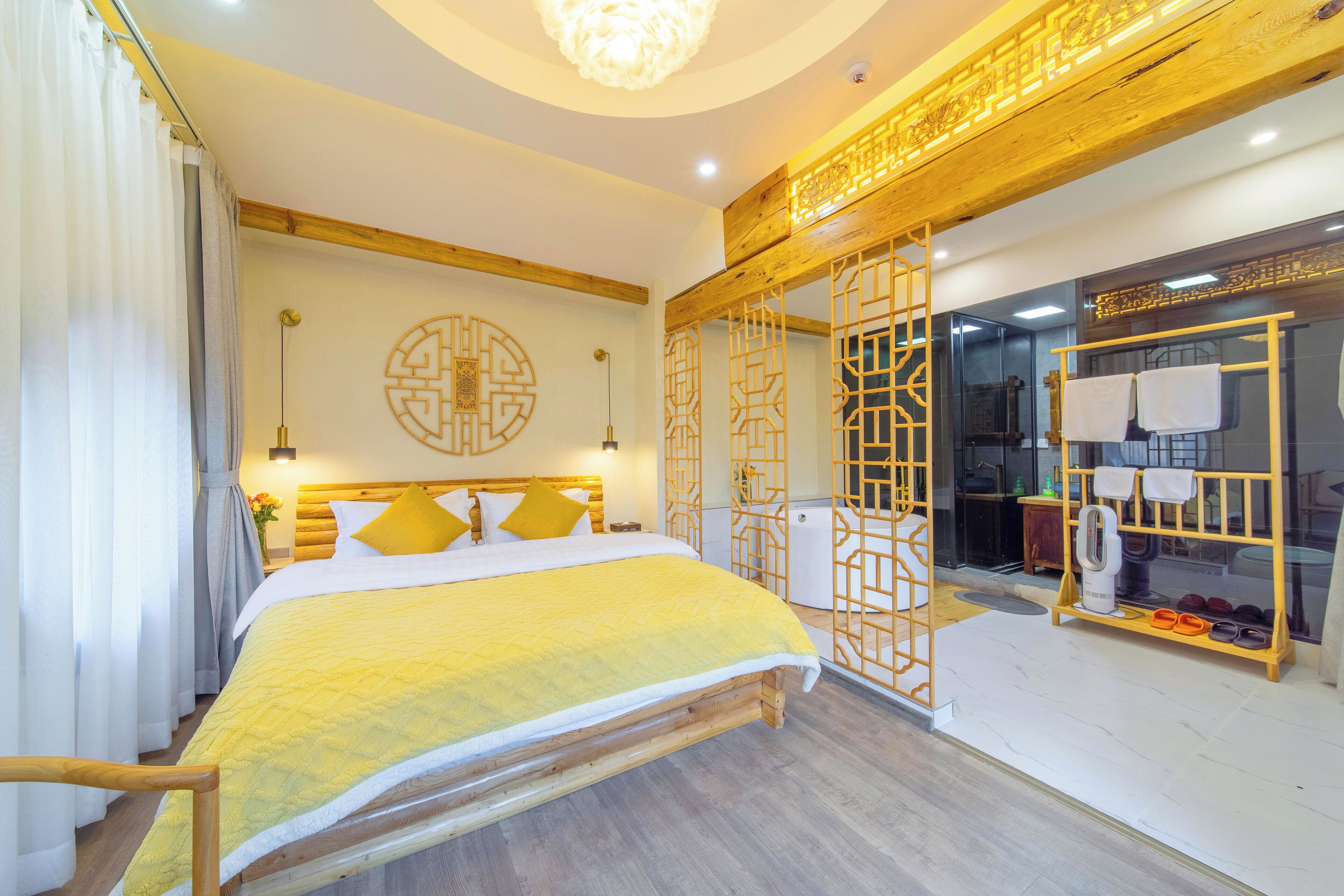 Habitación de hotel con una cama grande, cabecera de madera y un adorno en la pared. Se observa un zapatero con pantuflas variadas y un perchero con toallas.
