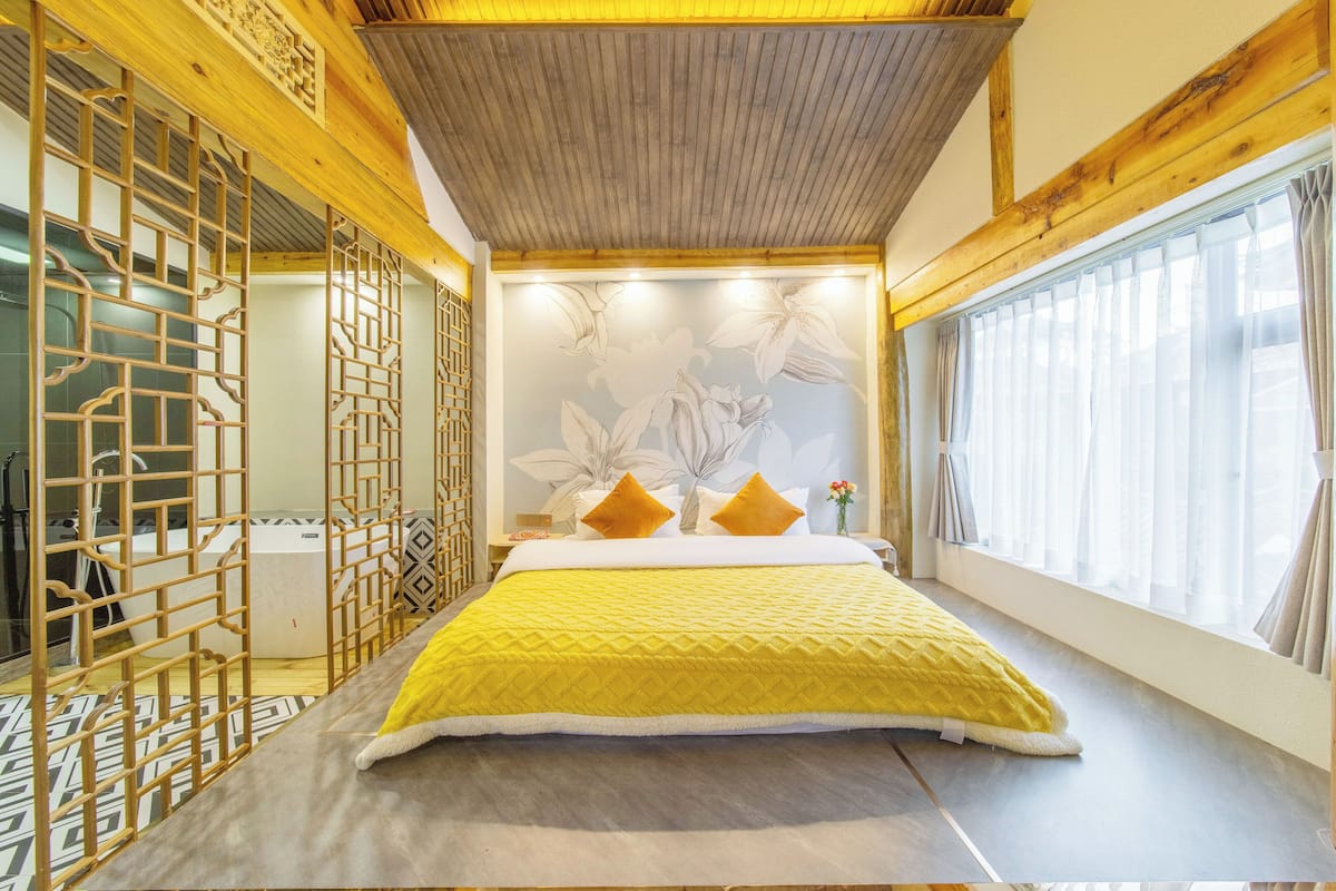 A modern bedroom with a large bed, wooden headboard, decorative wall paneling, and a window with curtains.