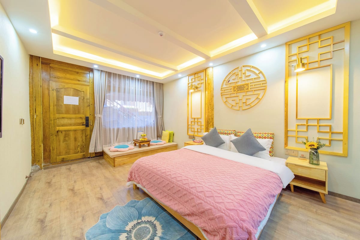 A bedroom with a large bed, wooden door, and a nightstand with a vase.