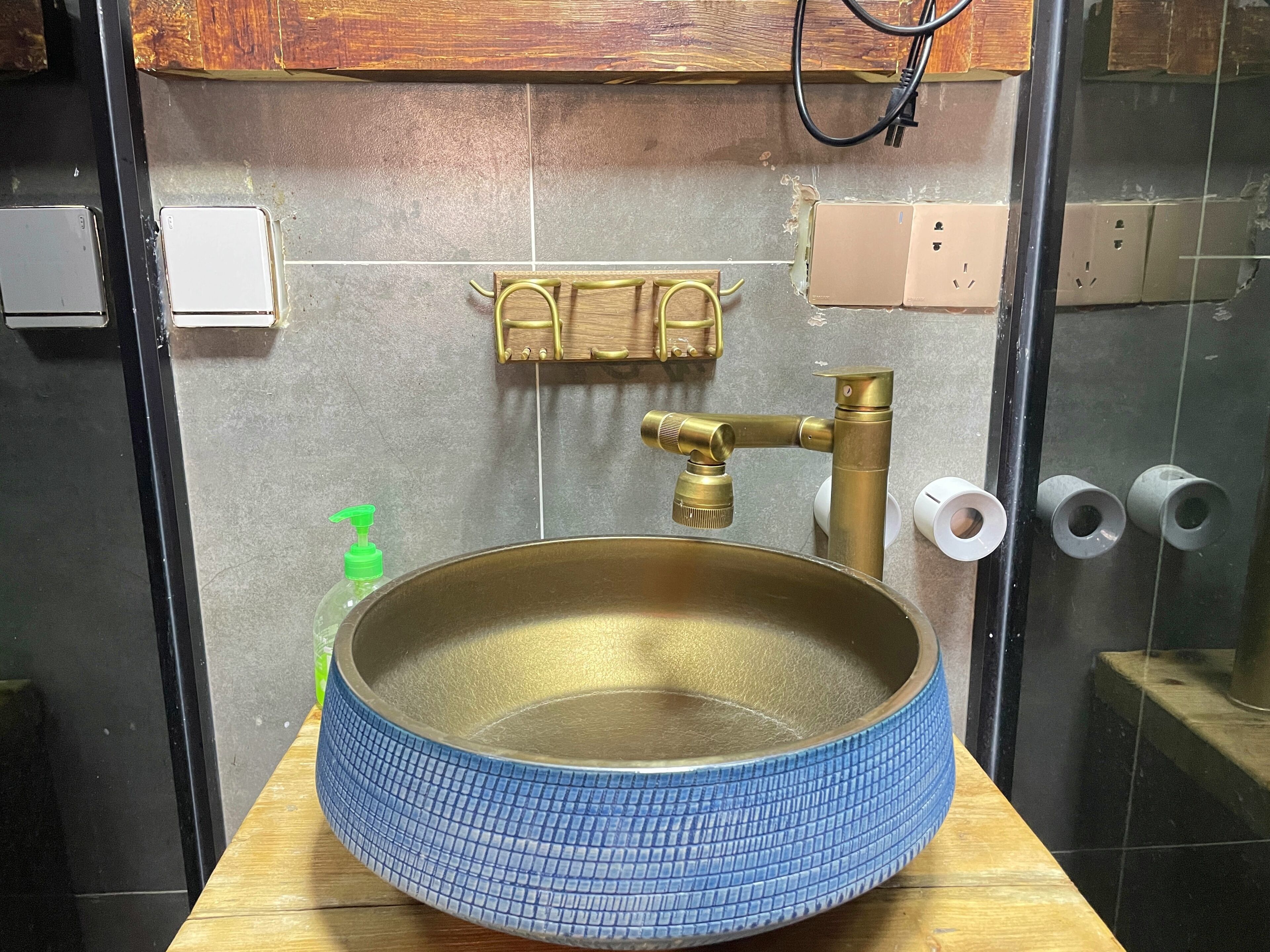Une salle de bain avec un lavabo rond bleu, un robinet en laiton et un meuble-lavabo en bois.