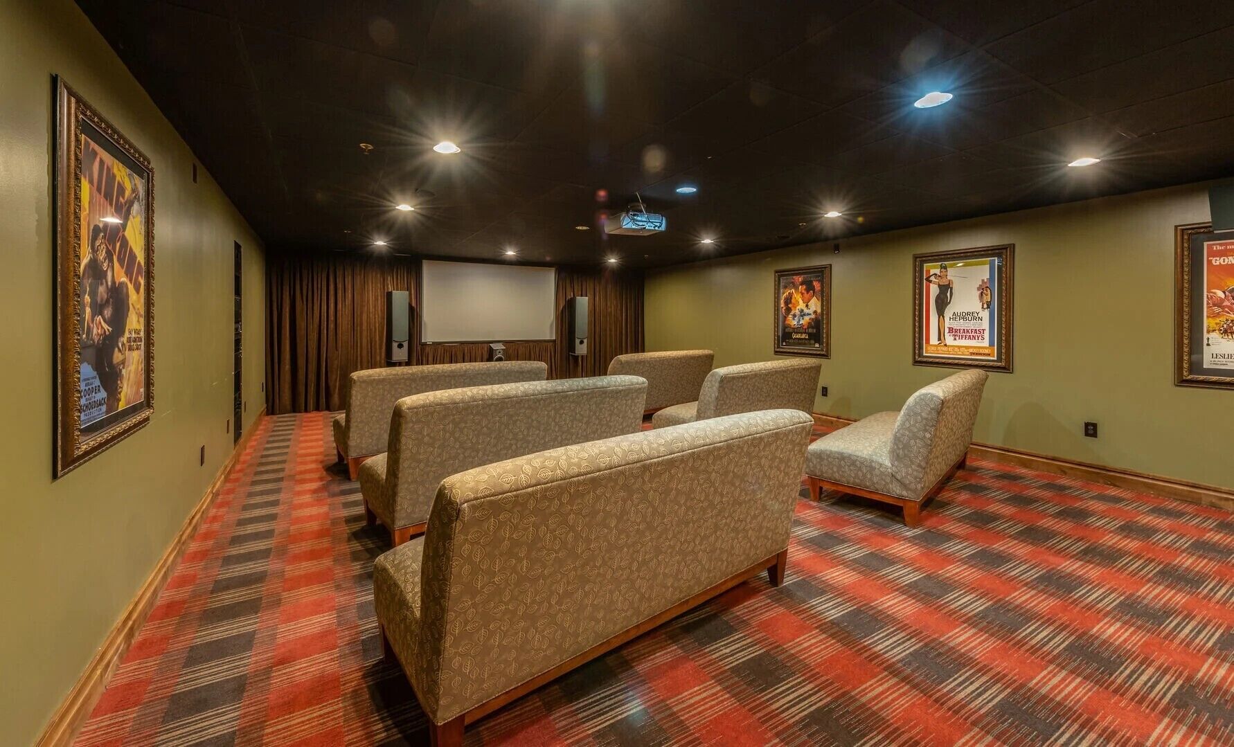 Una sala de cine en casa con alfombra a cuadros rojos y negros, varios sillones tapizados y carteles de películas enmarcados en las paredes.